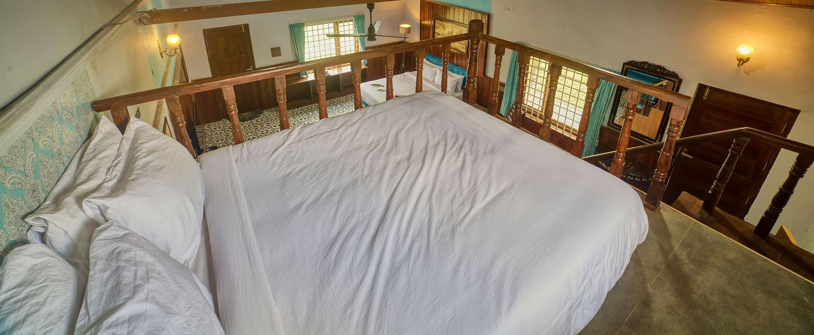 A loft bedroom with a white bed on an elevated wooden platform, featuring wooden railings and a sloped wooden ceiling. - Vintage Trails by Ilara