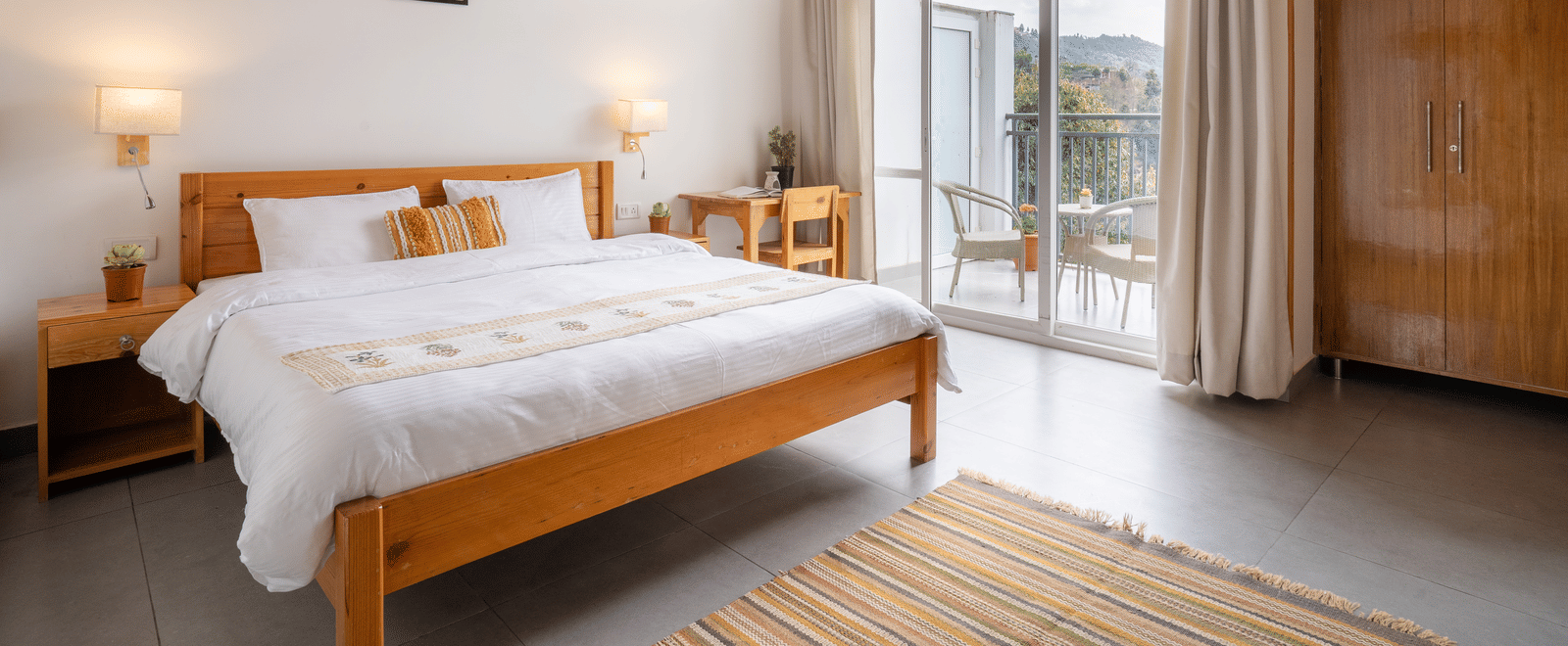A wide shot of a Ziran Retreat bedroom with a large bed, wooden furniture, and a floor-to-ceiling window looking out at a scenic view.