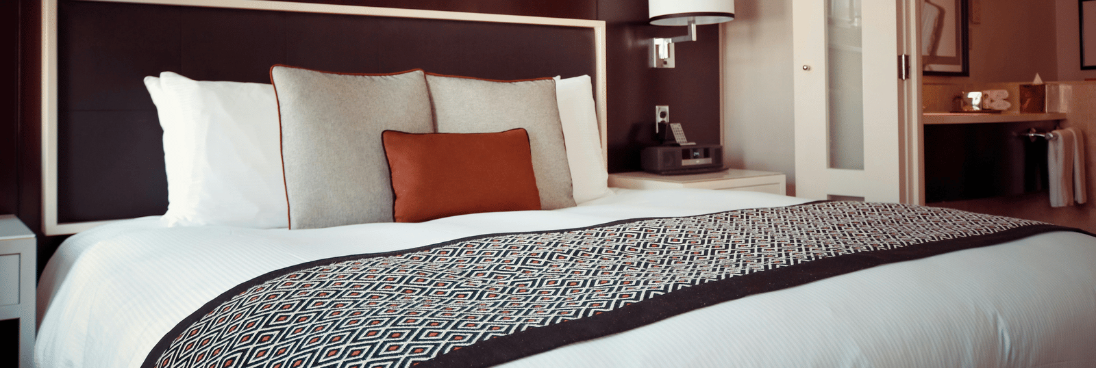 Modern hotel room with a large neatly made bed, stylish decor, and a view into the bathroom area.