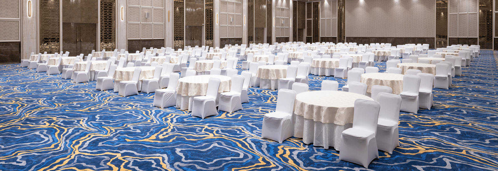 Grandis Ballroom set up with round tables and white linen seating under bright lighting at Merlis Hotel, Coimbatore