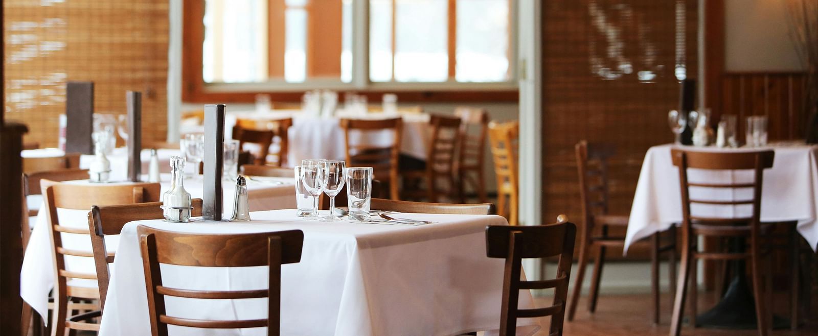 Interior of a restaurant with set tables, wooden chairs, and large windows, blurred for a sense of ambience.