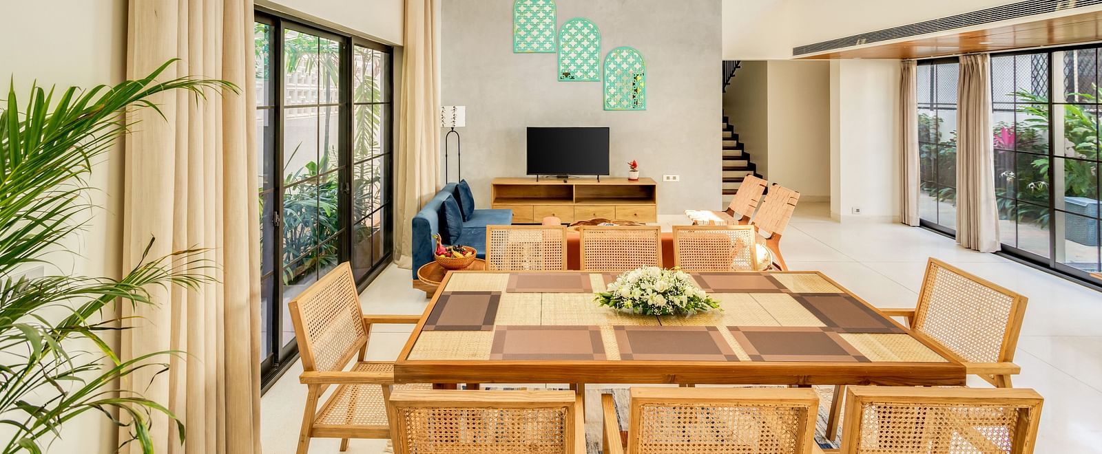 A bright and airy dining area featuring a large wooden table, modern chairs, and floor-to-ceiling windows with lush greenery outside - BluSalzz Villas - Alocassia, Anjuna