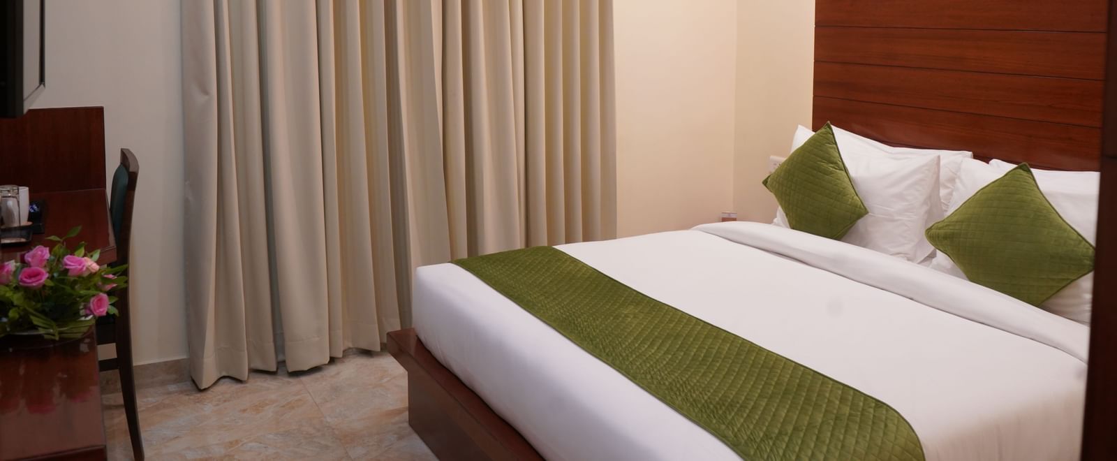 A wide shot of a hotel room bed with a white comforter and green accents, positioned between two bedside tables. 