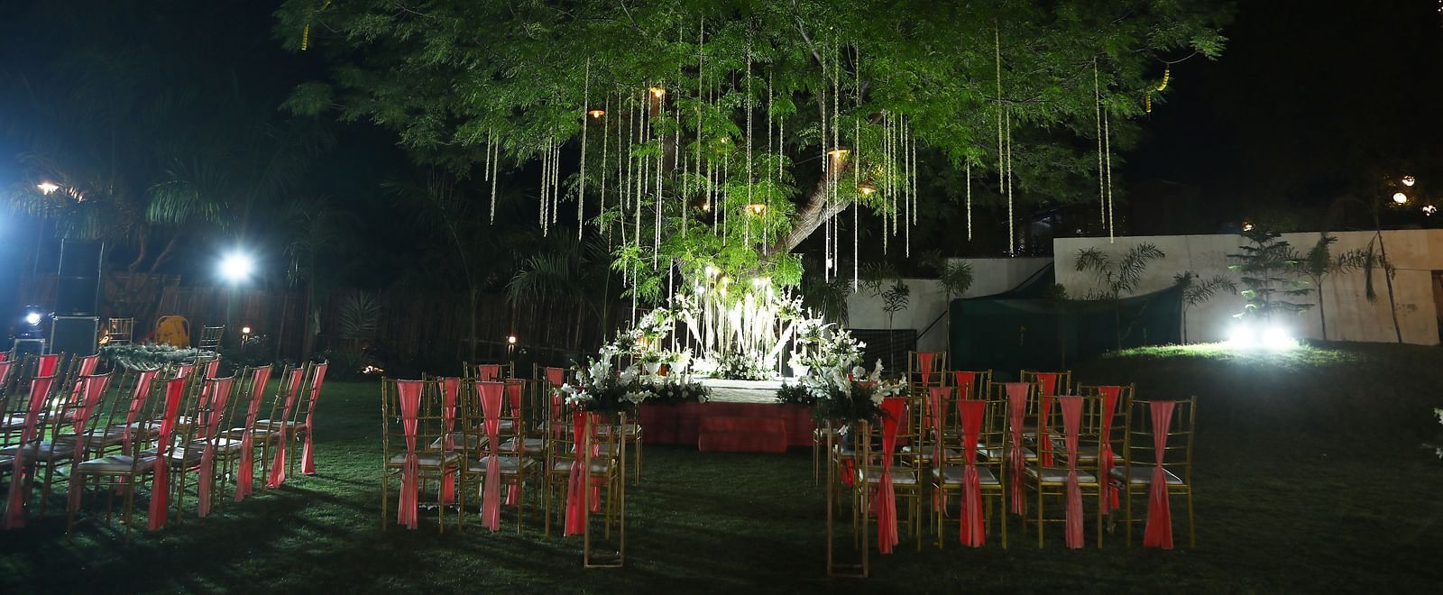 Nighttime event setup with chairs arranged under trees at Tisya Farms, Gurgaon.