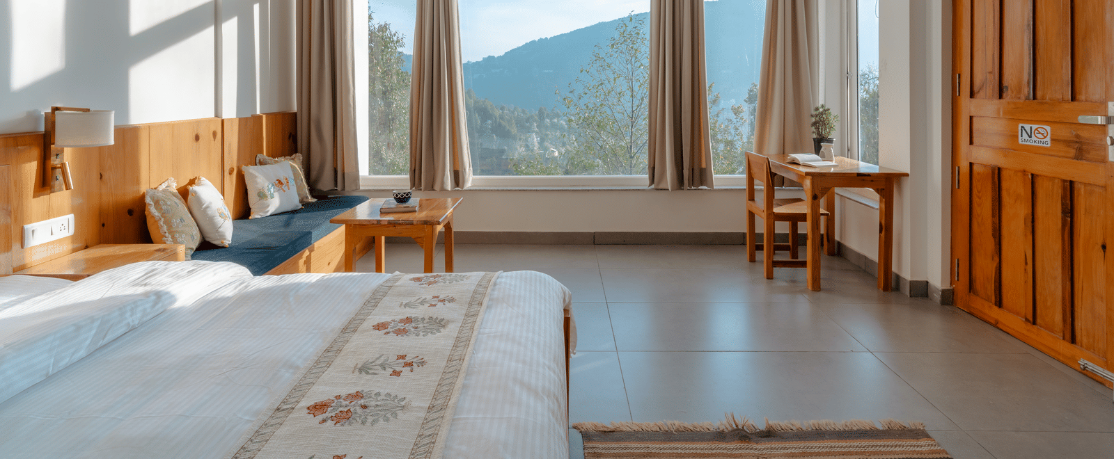 A bedroom at Ziran Retreat with a large bed, wooden furniture, and wide windows with a view of the mountains.