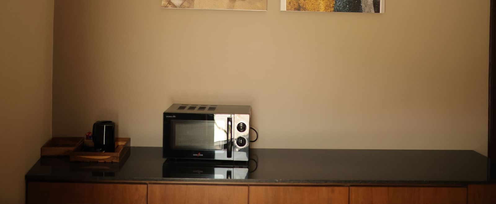 A microwave placed on a wooden table with a wall painting in the background at Luxury Villa with Plunge Pool at The Qualia Resort Club & Brewery, Udaipur.