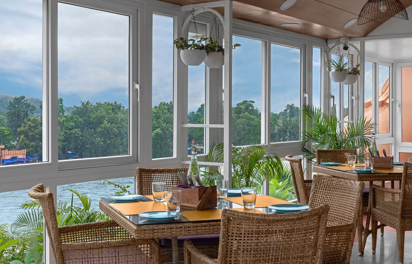 Indoor seating at The Patio café in Ganga Lahari, Haridwar with large windows offering serene views of the Ganges and lush greenery.