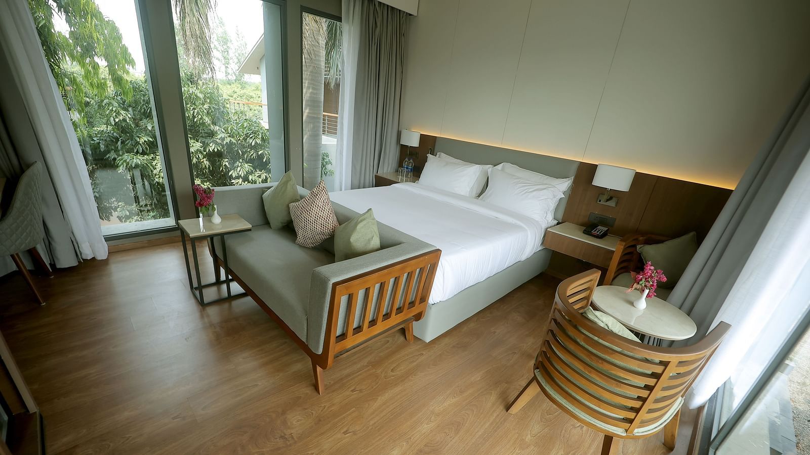 King size bed with green garden view through large glass doors and a cosy seating arrangement at Wyndham Garden.