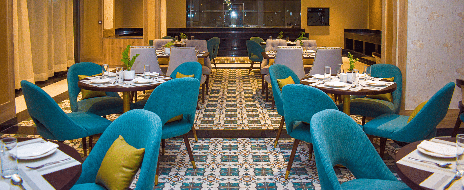 A modern restaurant interior with teal armchairs, round tables, patterned tile floor, and a distinctive globe chandelier - Urban Suites by BluSalzz, Jaipur