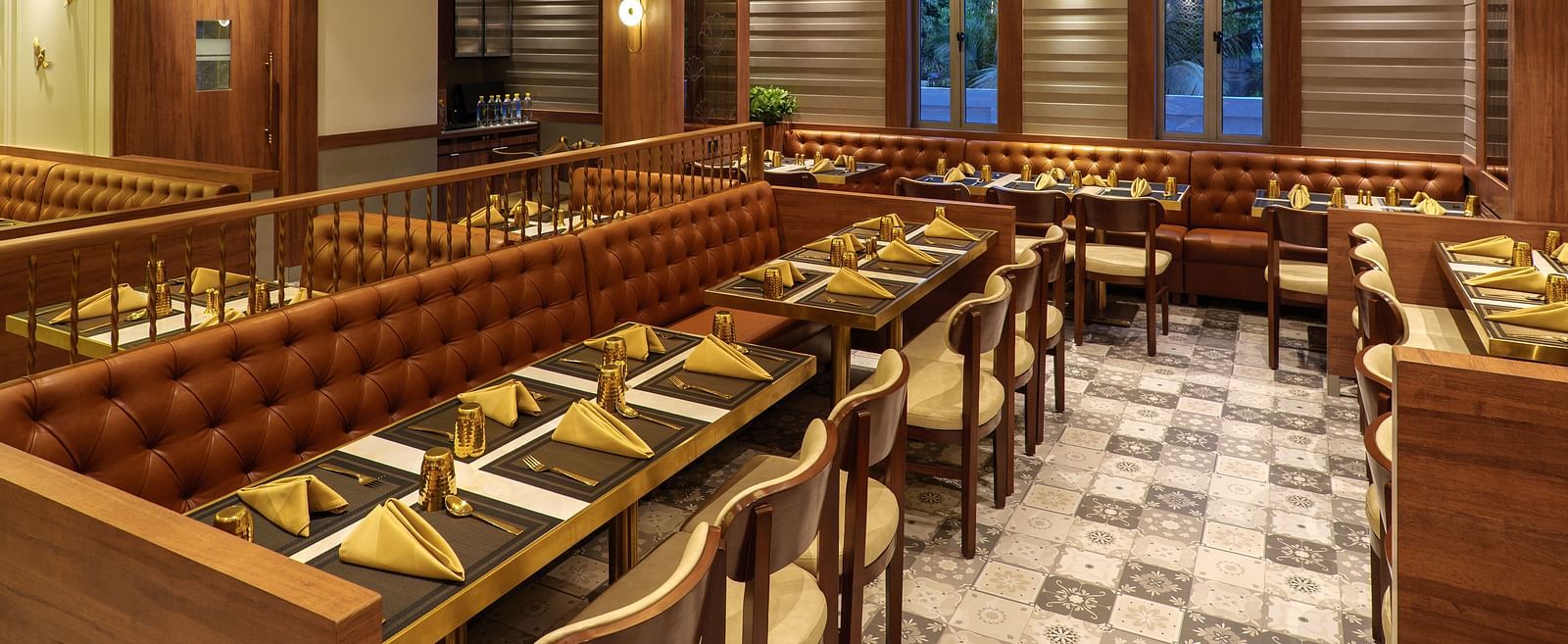 A warmly lit restaurant area features multiple tables set for dining, wooden accents, and decorative wall panels - Melior Inn