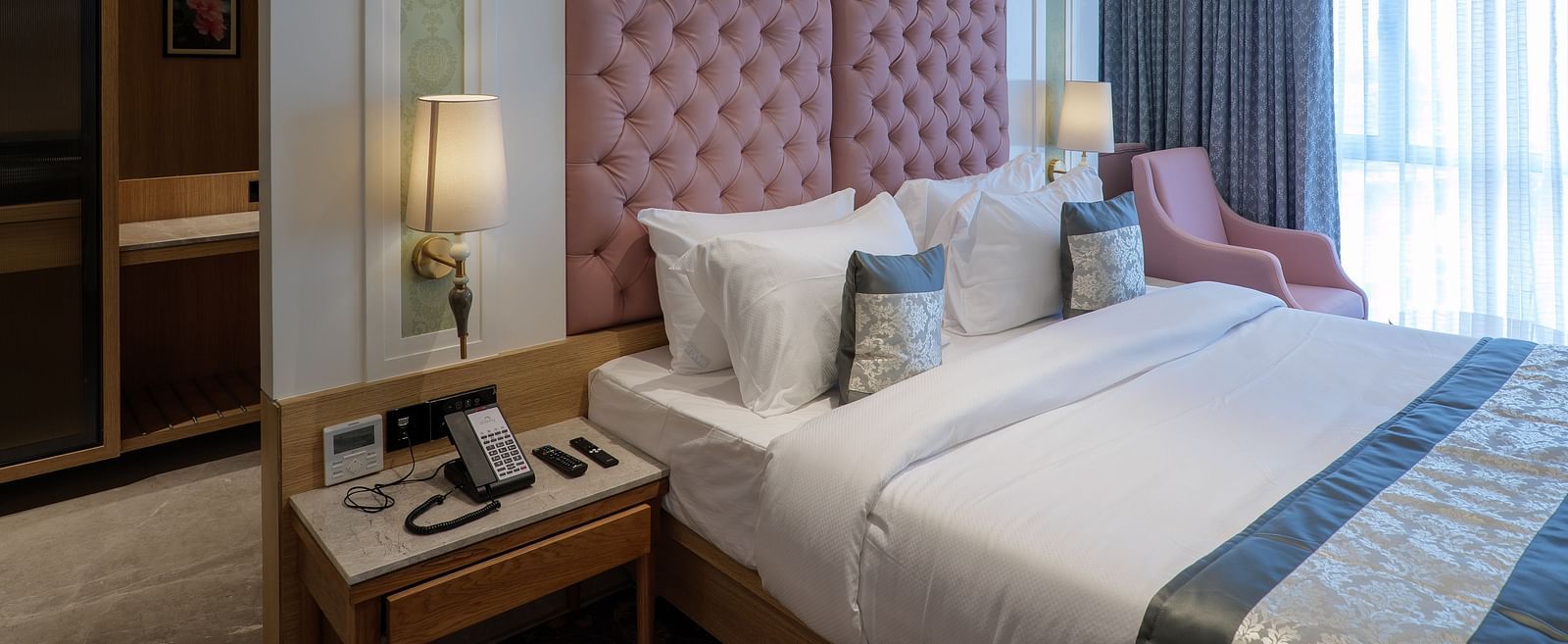 A room with a large bed featuring a pink tufted headboard, bedside tables, and an armchair with soft lighting - Melior Inn