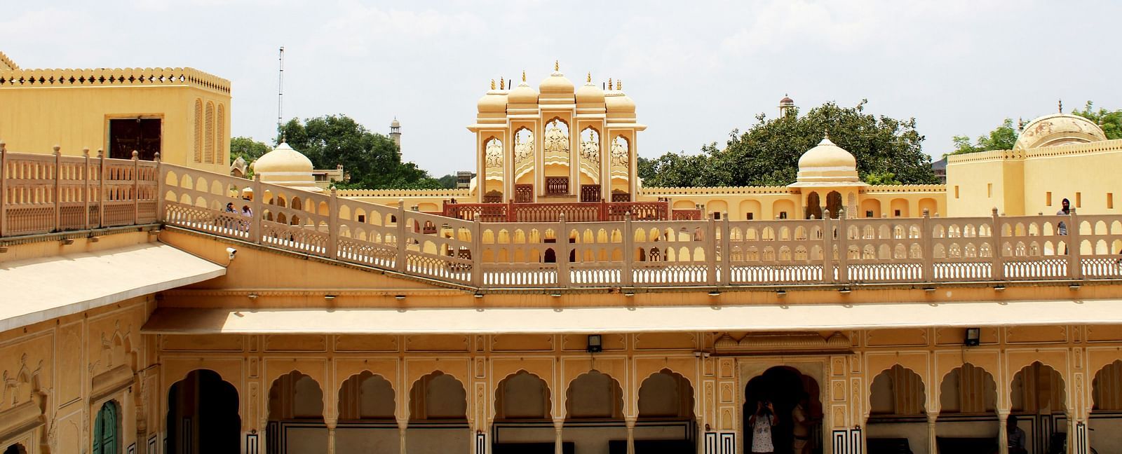 A sprawling yellow palace complex with ornate arches and balconies under a bright, cloudy sky.