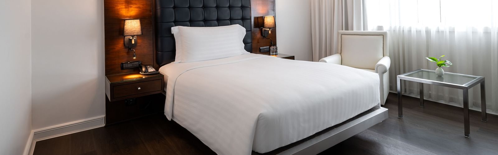 Minimalist bedroom with dark headboard, white linens, and window seating at Night Hotel Bangkok.
