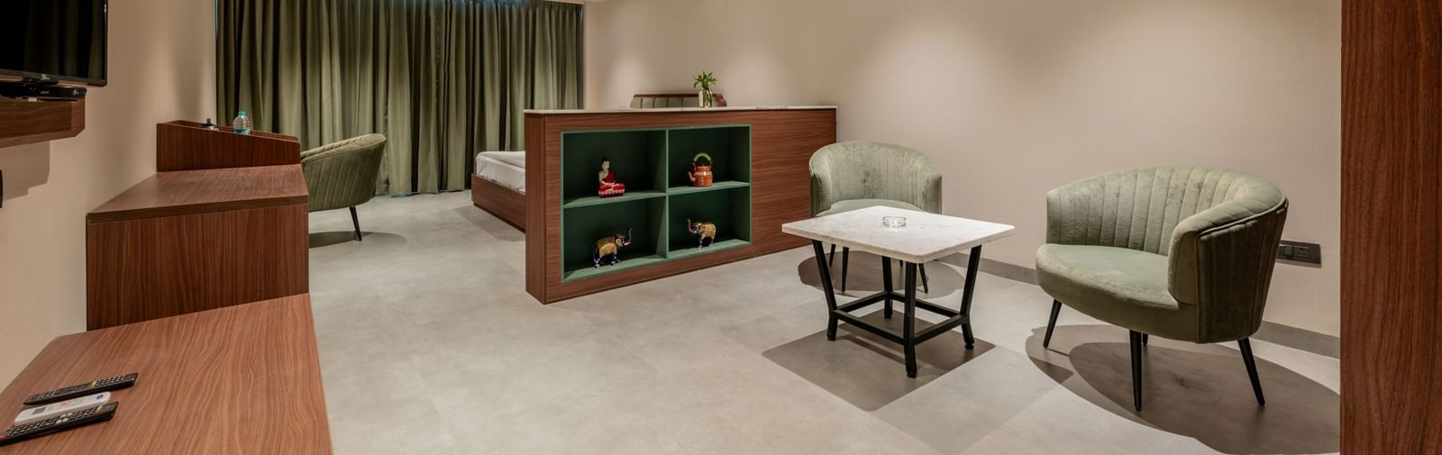 A room with large bed, a study desk, cushioned chairs, and partition shelf under ceiling fan at Hotel Highway King, Neemrana.