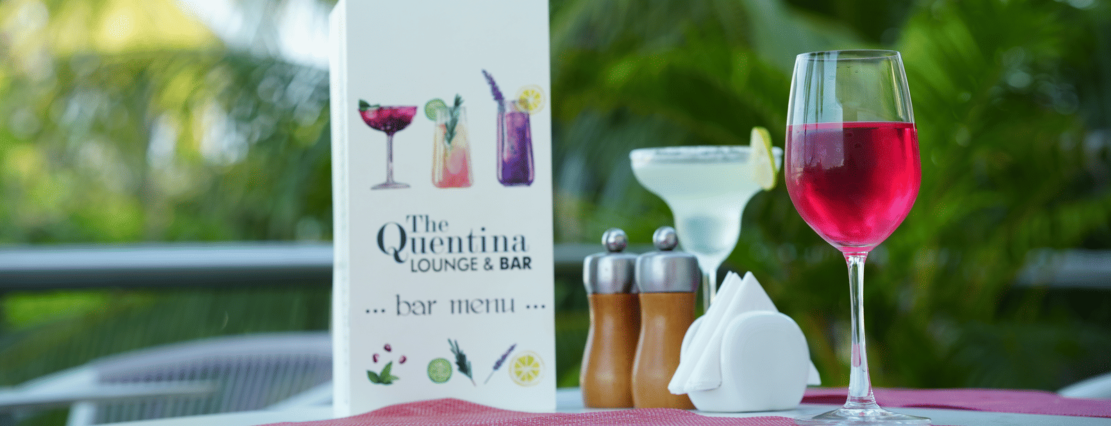 Outdoor table with a menu card, a red drink, a white drink and condiments at Grande Bay Resort & Spa.