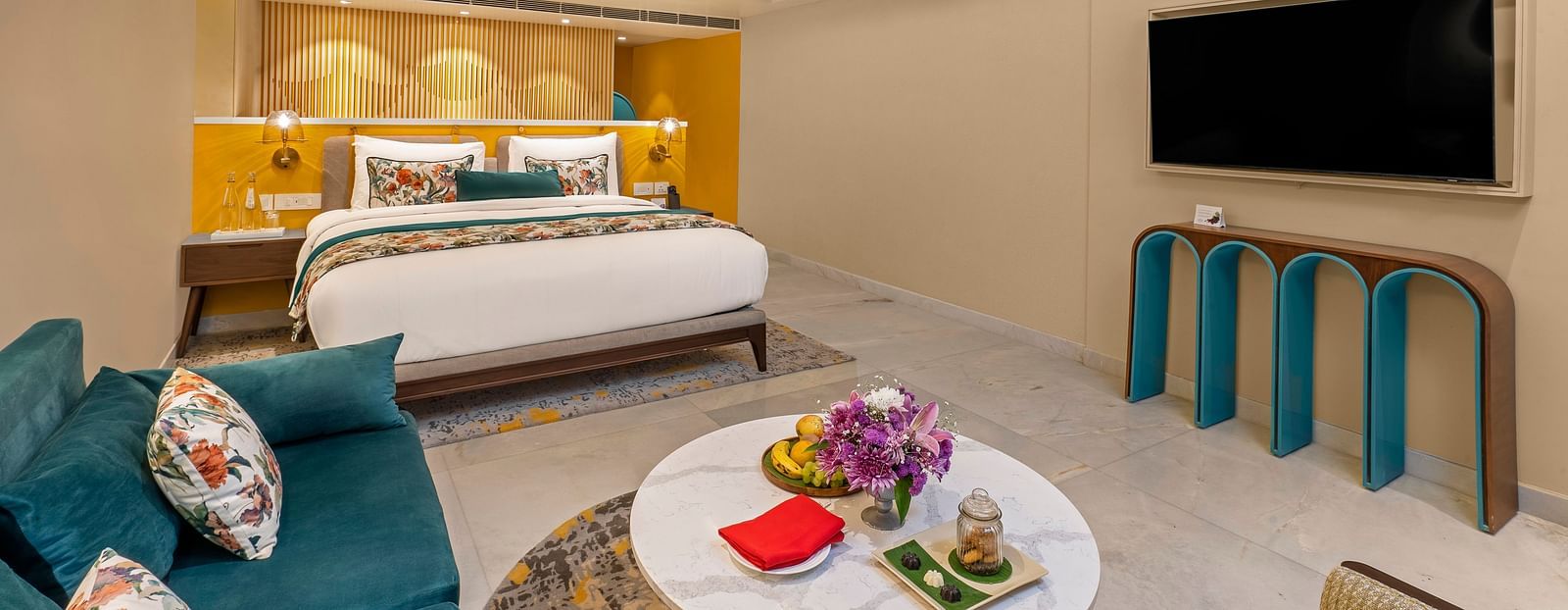 A n image of luxurious hotel suite with king bed, sofa, coffee table, and stylish decor.