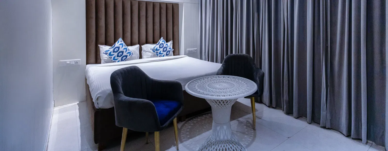 Deluxe Room featuring a king size bed with patterned cushions, two chairs, a table, and curtains. - Hotel Downtown17, Chandigarh