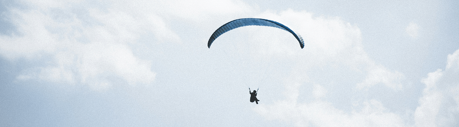 A view from below of a person paragliding with blue sky in the background