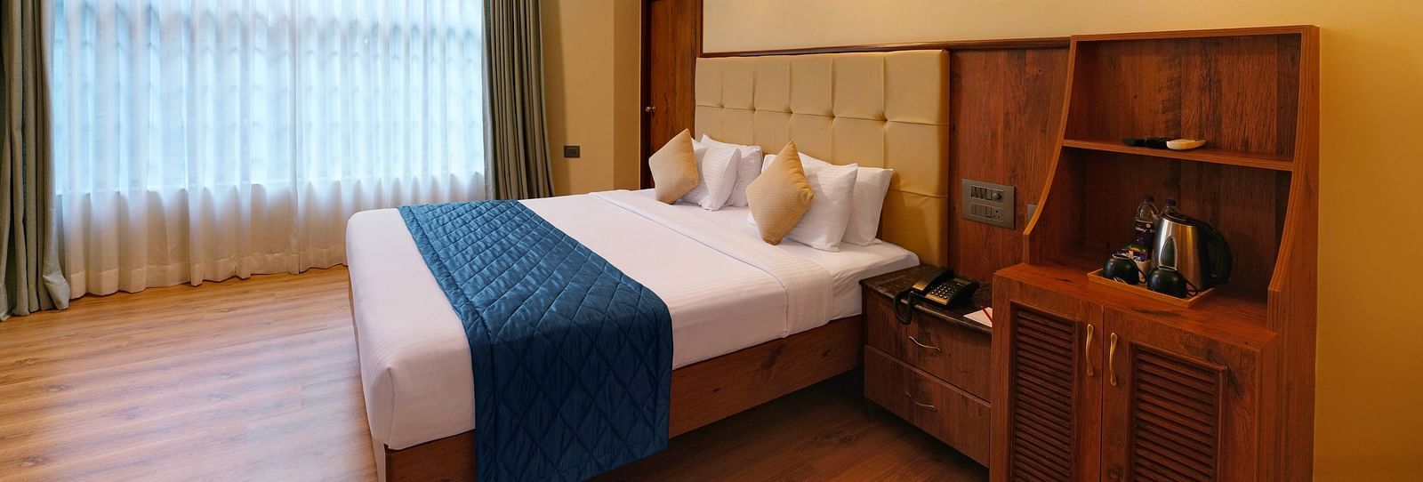A room in bengaluru with large windows, a queen size bed, and wooden decor - Cross Roads Inn, Bengaluru