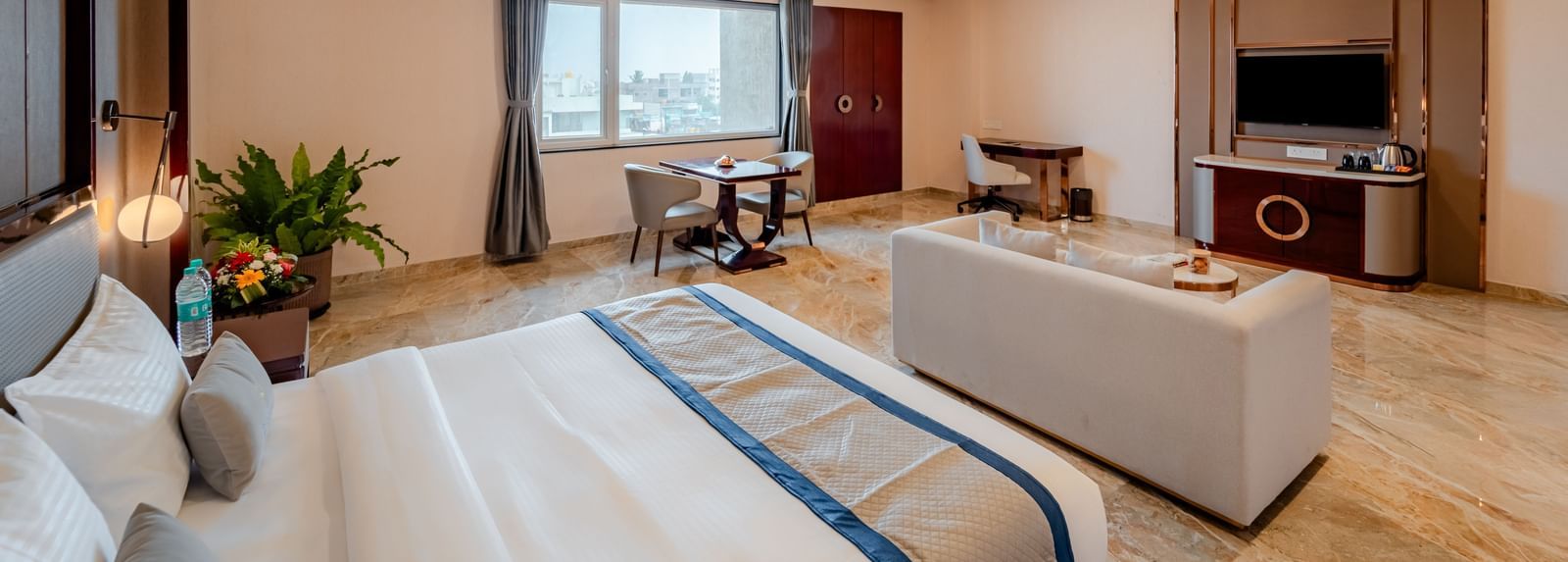 Spacious suite featuring a comfortable bed, lounge area, and city views | Suite | Pravasa Hotel, Vijayapura