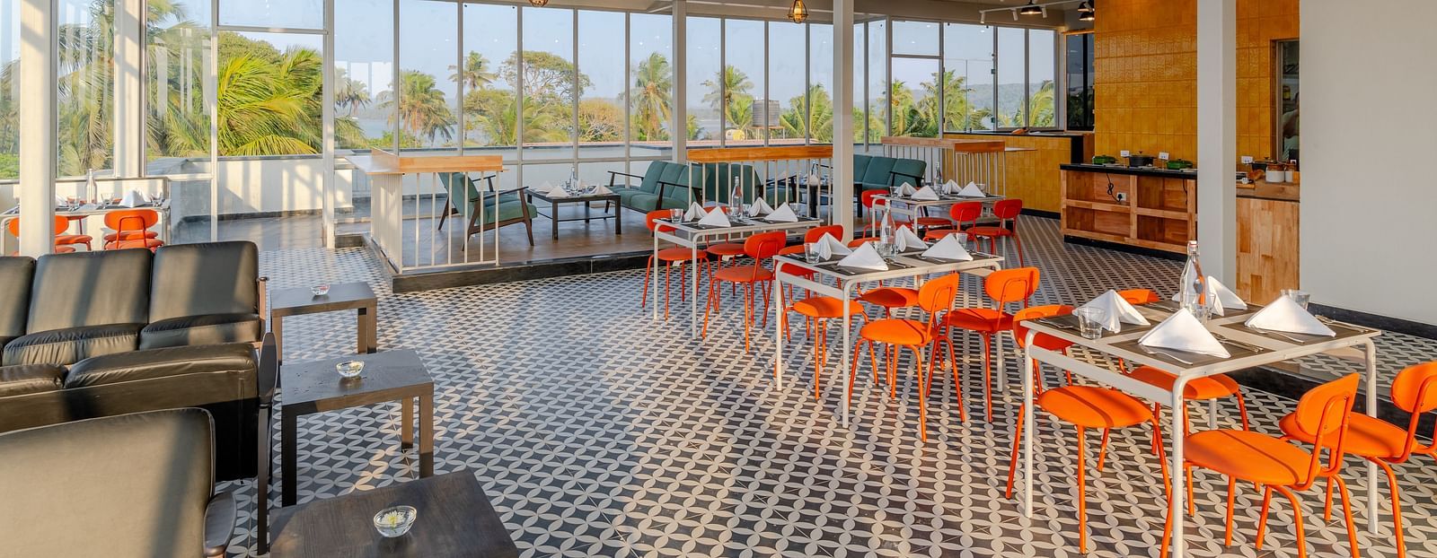 spacious and airy restaurant with industrial-style exposed ceiling, large windows letting in natural light, and a color palette of orange and grey, providing a relaxed dining atmosphere  at Bedzzz Xclusiv Morjim, Goa
