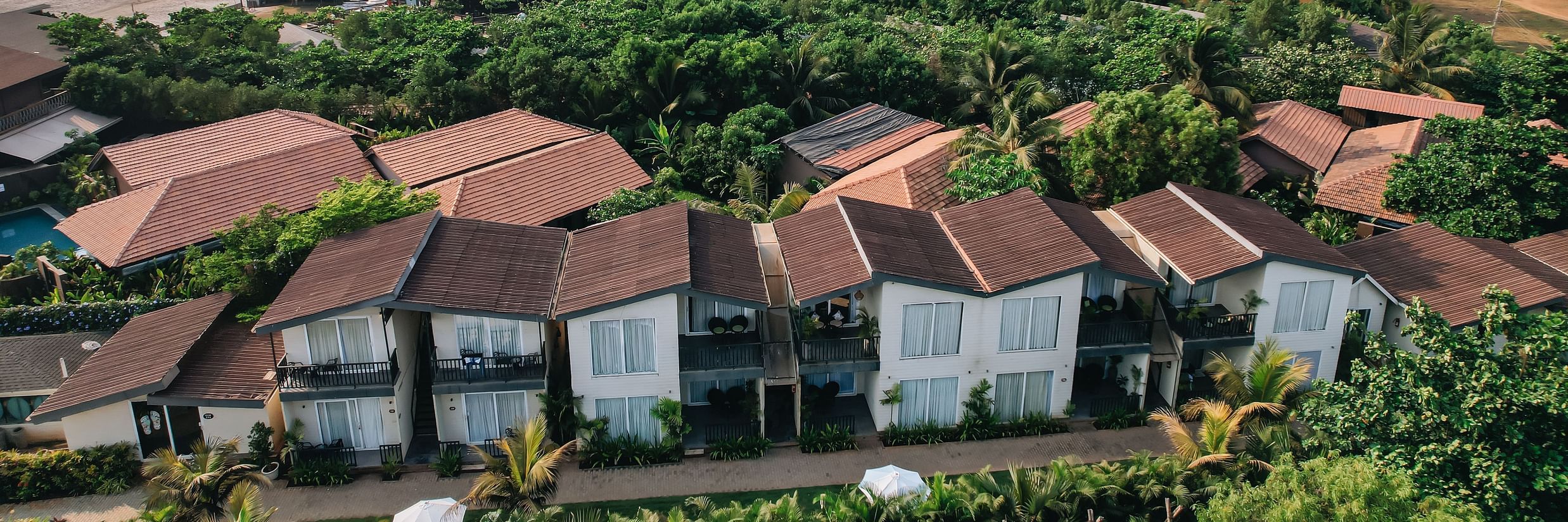 an aerial vie image of the facade of sibaya beach resort, morjim beach that is surrounded by lush tropical greenery