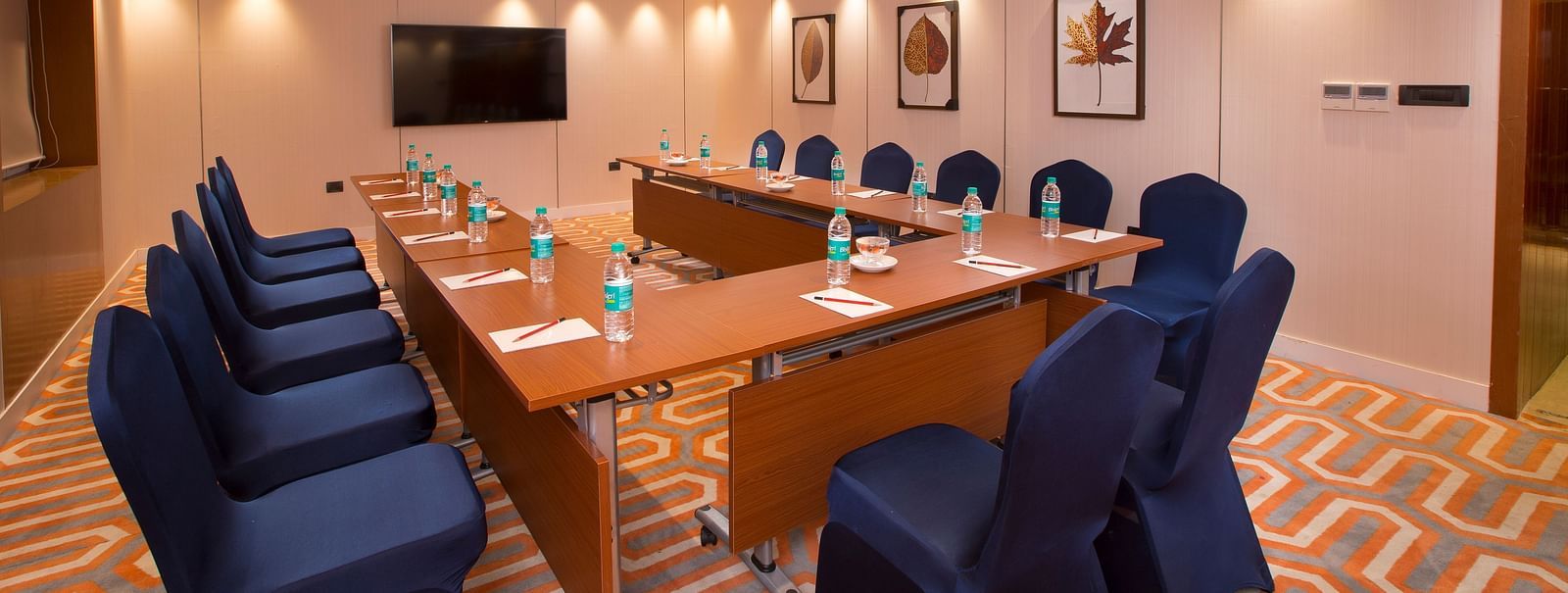 A formal boardroom with blue chairs around a long table, a flat-screen TV on the wall and framed leaf prints - Hotel Southend by TGI - Bommasandra, Bangalore