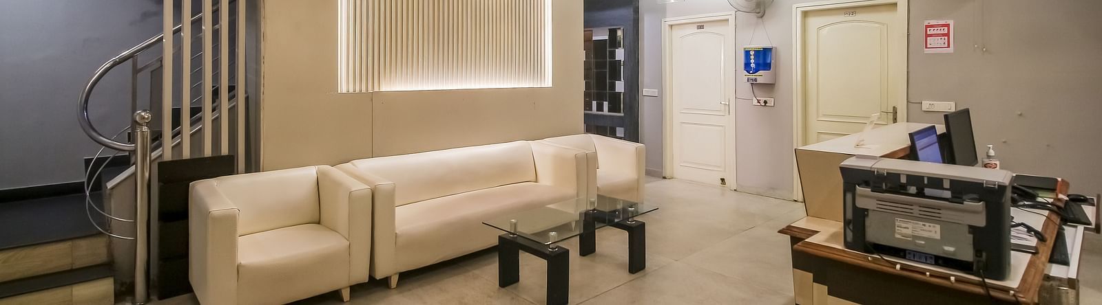 A hotel lobby with a seating area featuring white sofas, a textured wall with lighting, a spiral staircase, and a reception desk with equipment. - Hotel Diamond Plaza, Chandigarh.