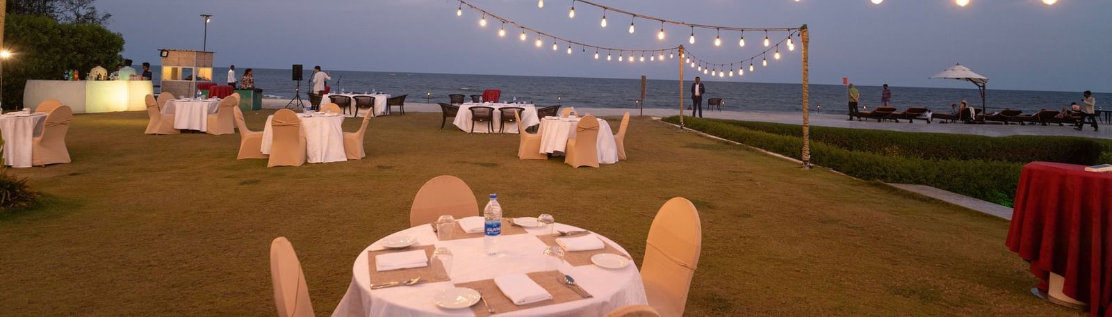 Round tables with white chairs set up on a lawn under string lights - Kaldan Samudra Palace