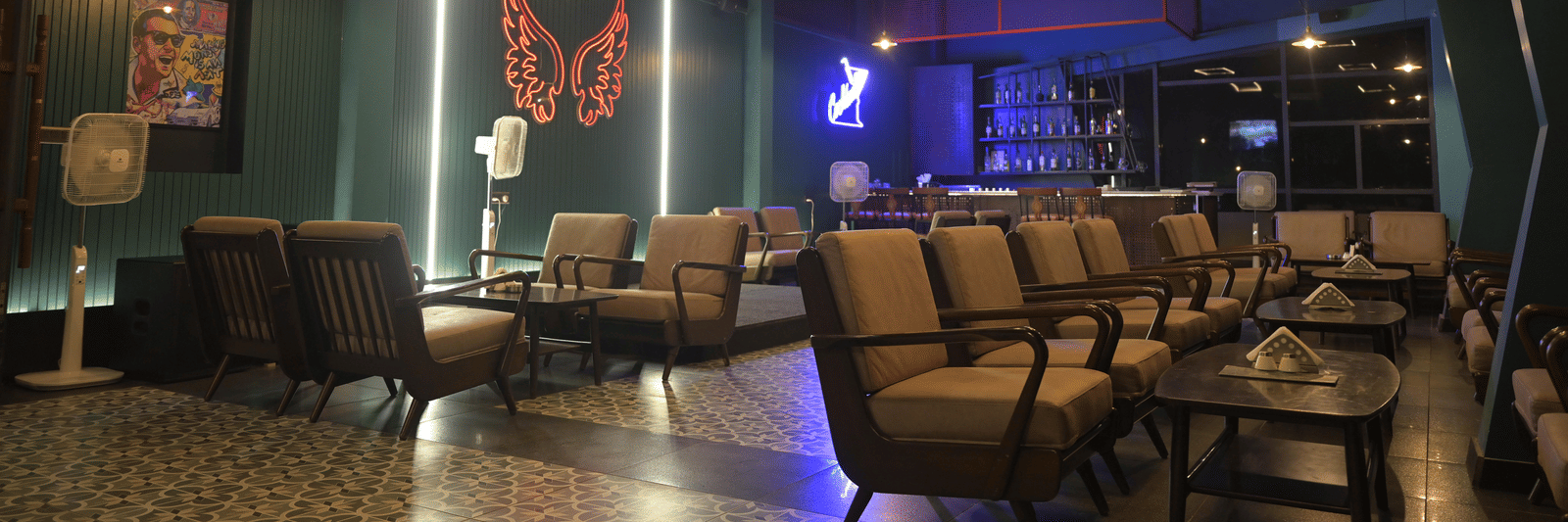 A cosy lounge setting featuring cushioned chairs and a neon butterfly wall installation glowing in the background at Hotel Sonar Bangla Mayapur.