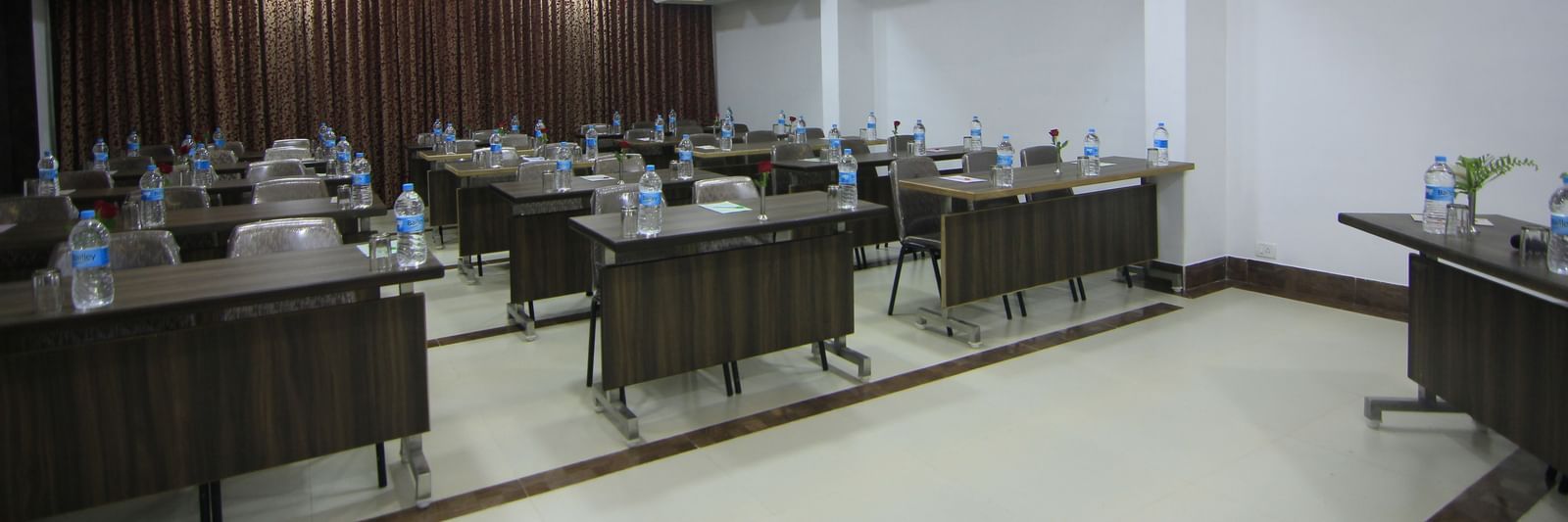 Conference room at Krushnai Resort with long rectangular tables arranged in class room style with chairs around them and a water bottle on each table.