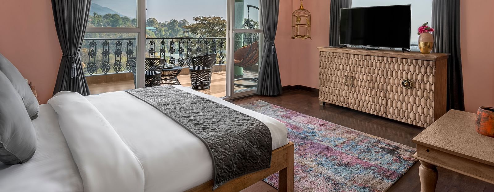 a bedroom with large windows leading out into the balcony and a large bed facing a television - Atman, Dharamshala