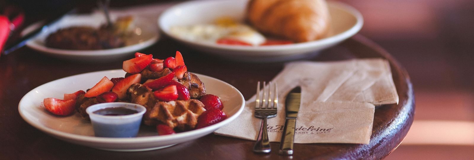 Waffle with strawberries and a croissant served on a round coffee table in a cafe. 