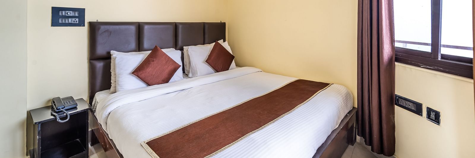 a room at Flutter Hotels & Resorts featuring a bed and a telephone placed on the side table
