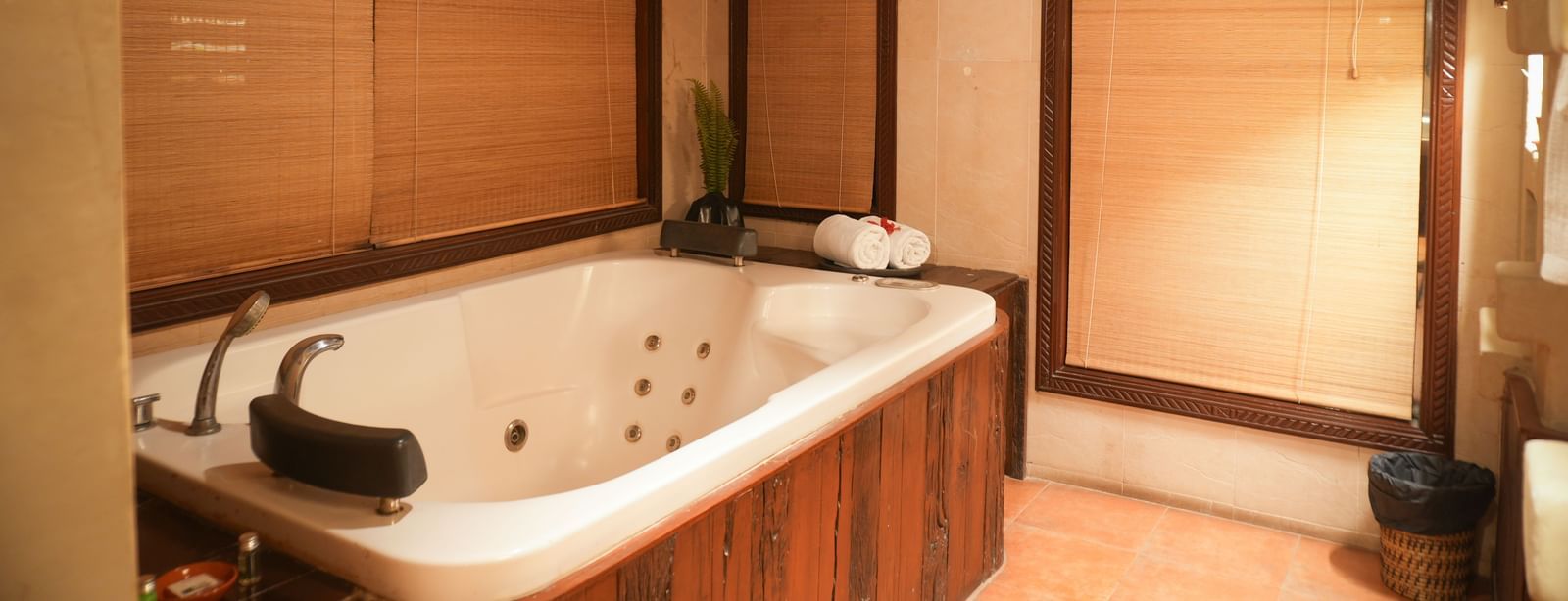 Wooden panelled jacuzzi in the Zamindar Suite at Vedic Village Spa Resort, set against brown flooring and brown roll-down blinds.