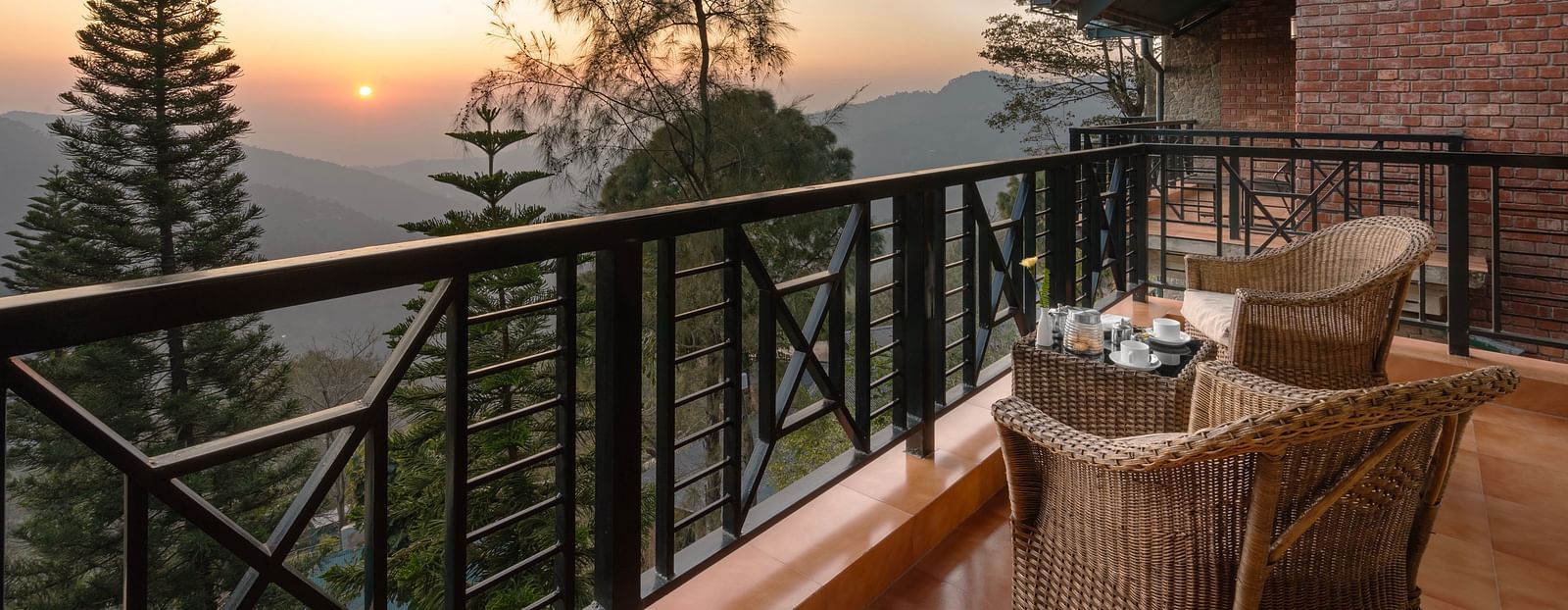 Two wooden chairs and a table set on an open balcony with a sunrise view - Baikunth resort, kasauli 