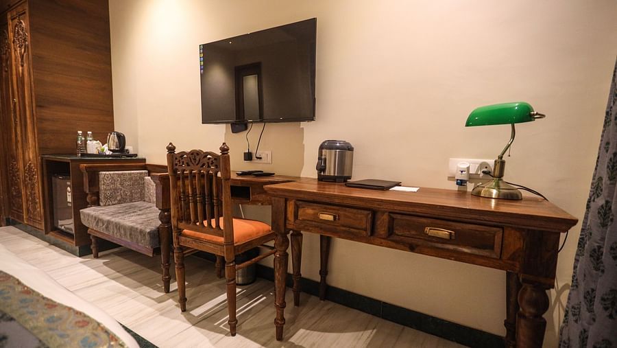 Spacious room with a wooden table and chairs, a wall-mounted television, and essential items on the table | Panna Vilas Udaipur