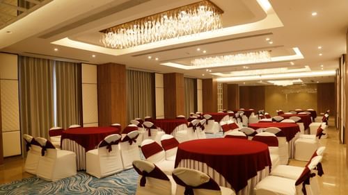 A banquet hall in Zirakpur with round tables, carpeted floors, and warm lighting - Tulip Inn, Zirakpur
