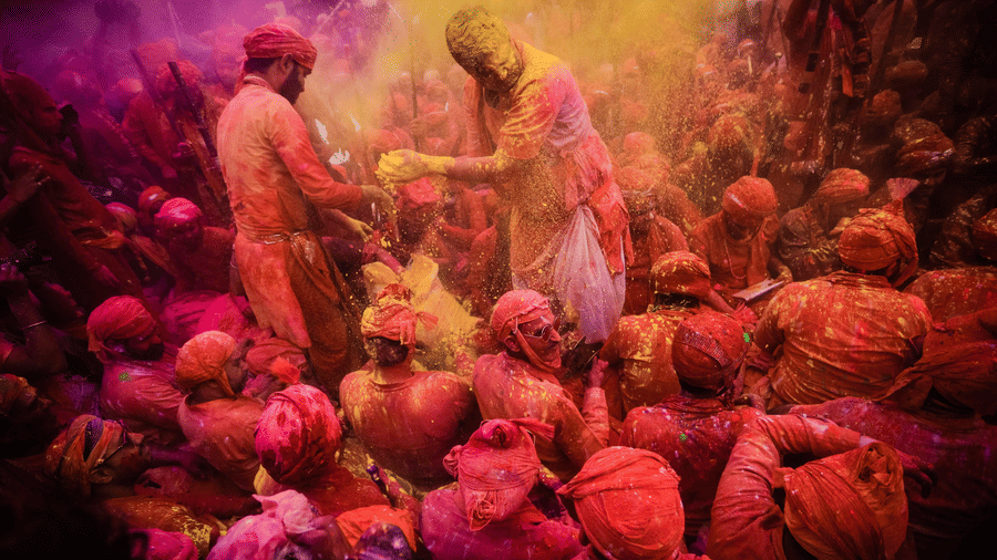 Group of people standing close together during Holi, covered in coloured powder and facing one another.