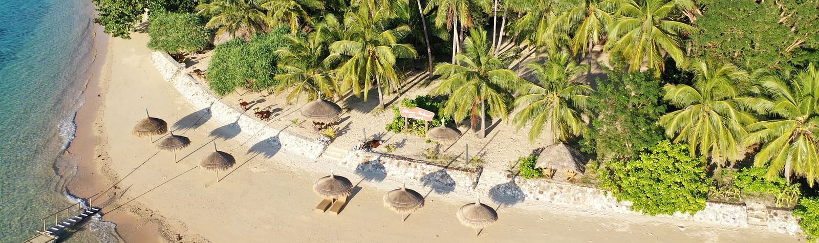 Aerial view of beach loungers and thatched umbrellas along shoreline at Flower Island Resort.