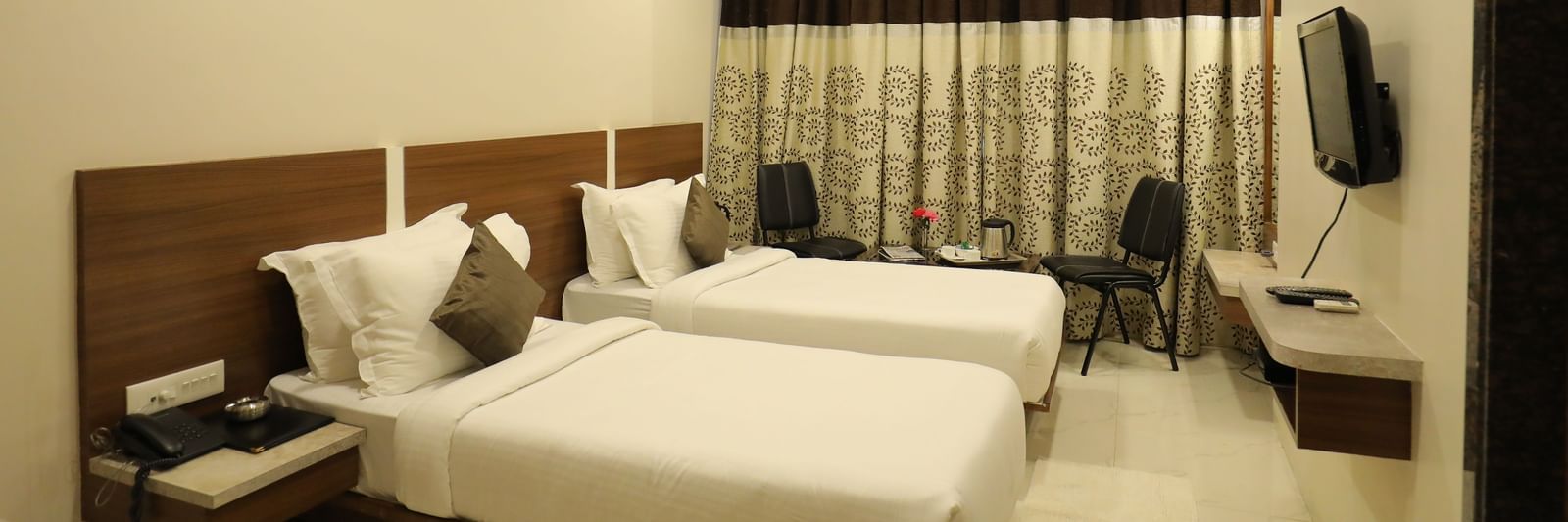 Side view of the Super Deluxe Rooms that are furnished with twin beds, wall-mounted TV, a seating area for two, and drawn curtains at Highland Resort.