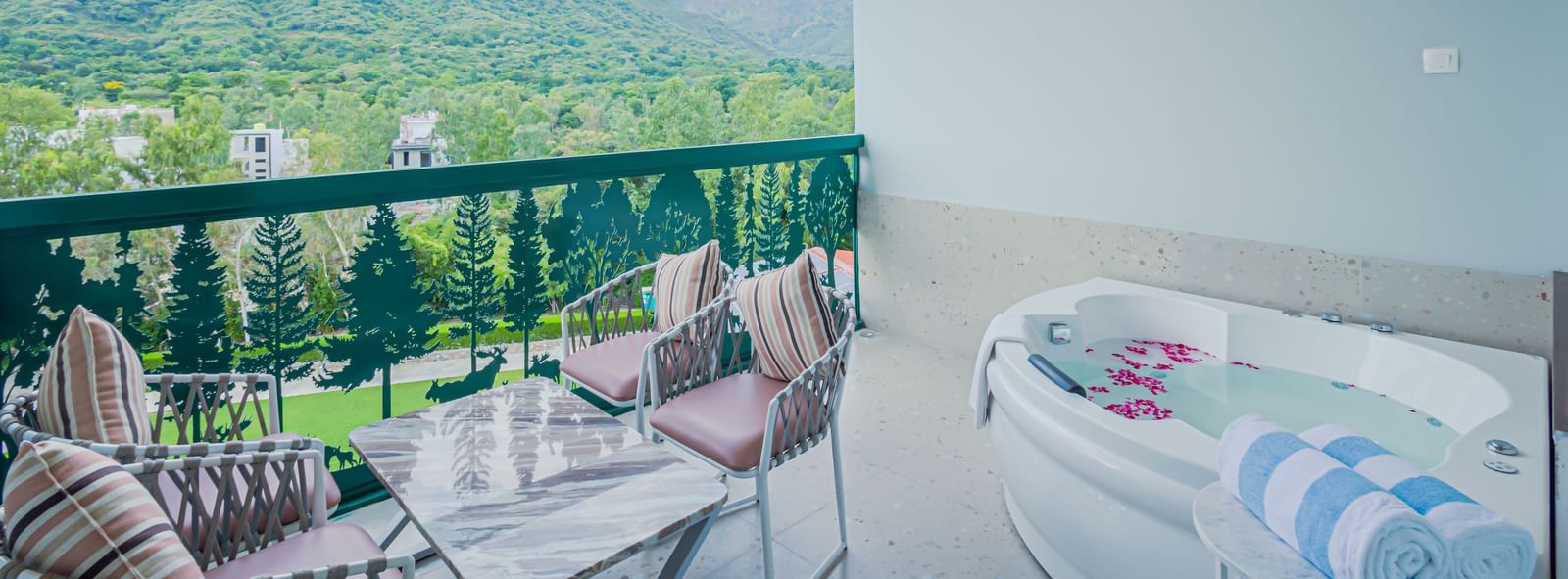 A balcony of Sajjan Villa at Bamboo Saa Resort and Spa, Udaipur featuring a seating area with chairs and centre table and a bathing tub near to it with towels.
