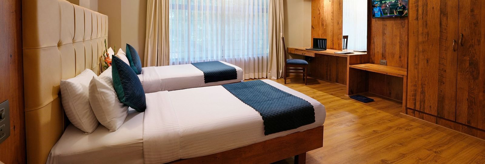 An elegant room featuring twin beds and wooden furnishings - Cross Roads Inn, Bengaluru