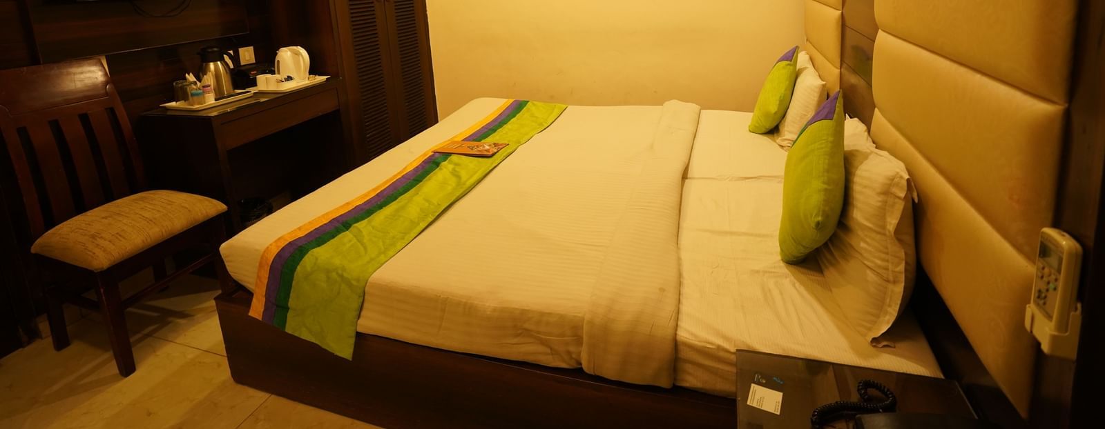 Standard Room furnished with a bed featuring white linens and green and yellow accents, two pillows, a chair, a desk, a television, and a wardrobe. - Hotel Dreamland, Chandigarh