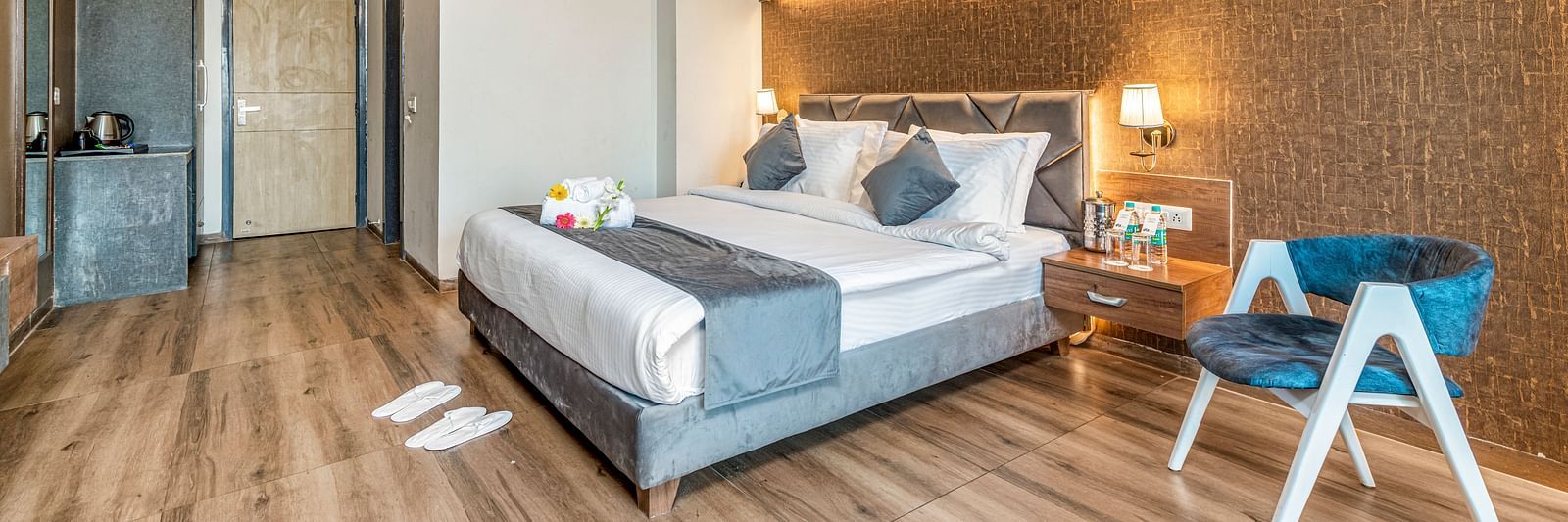 An image of the deluxe room at DLS Ganga Bliss, Haridwar featuring a bed, bed side tables, a chair, and other room amenities