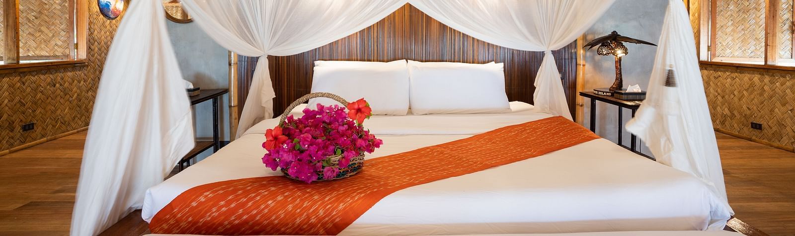 Close-up of a bed with white canopy netting and a folded towel with flowers on the bed at Flower Island Resort.