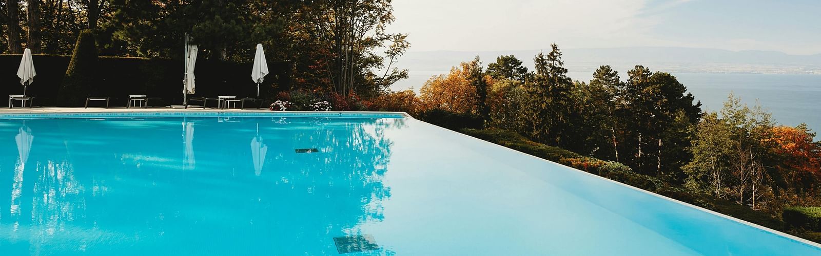 An image of a swimming pool with the backdrop of lush greenery and a bright sky