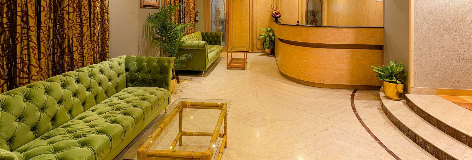 A cosy reception area with green couches and warm lighting - Cross Roads Inn, Bengaluru