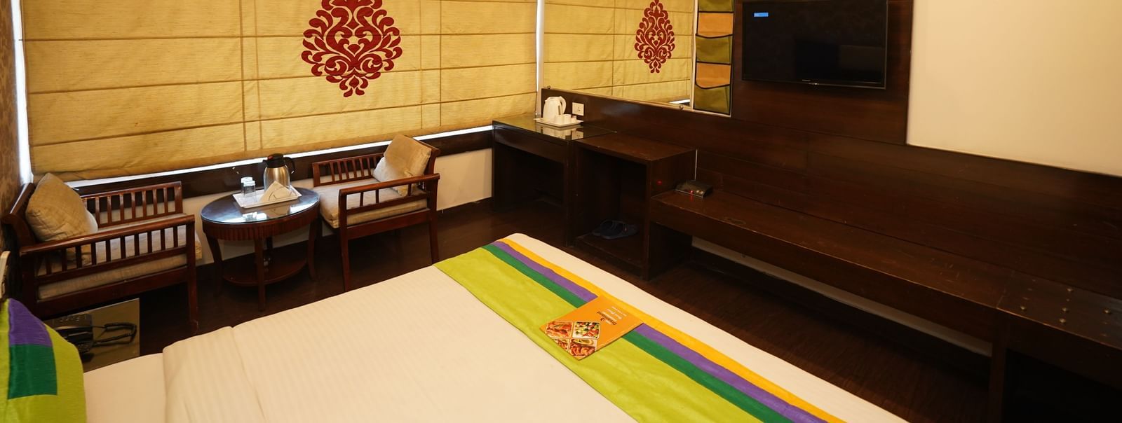 Spacious Deluxe room in Hotel Dreamland, Chandigarh with wooden floor, two seating chairs with tea table and comfortable king-sized bed.