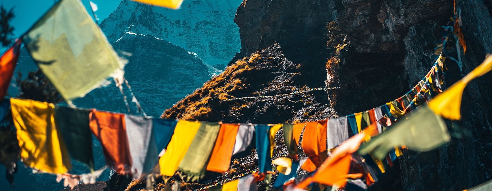 Colorful prayer flags strung across a mountainous backdrop with a clear sky